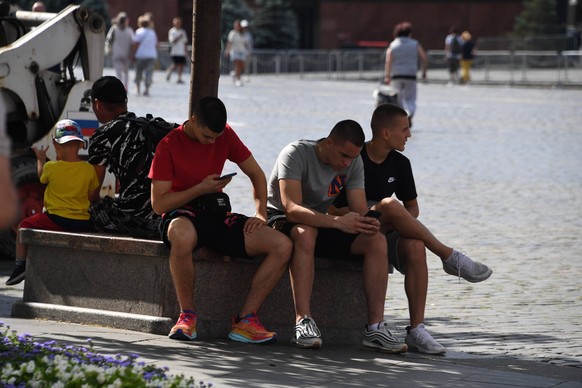 Moscow. Young people sitting in the shade with a mobile phone. KomsomolskayaxPravda