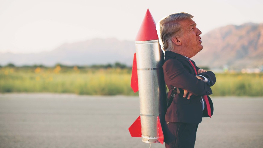 A young business minded boy is wearing a business suit, space helmet with a rocket strapped to his back. His hands are on his hips and he is smiling at the camera standing on blacktop. Plenty of copy  ...