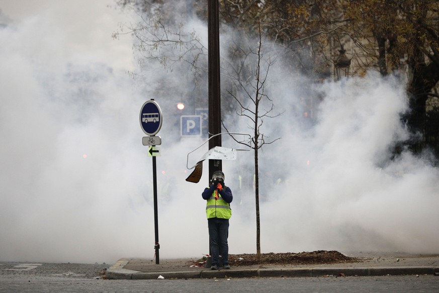 A demonstrator uses his phone amid tear gas near the Champs-Elysees avenue during a demonstration Saturday, Dec.1, 2018 in Paris. French authorities have deployed thousands of police on Paris' Champs- ...