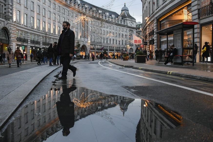 A man wears a face mask while he walks and is reflected into a puddle in Regent Street, ahead of the new Tier-4 restriction measures, in London, Saturday, Dec. 19, 2020. Britain's Prime Minister Boris ...
