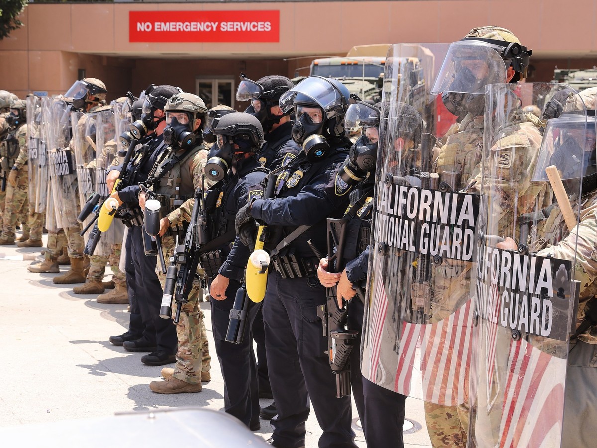 08.06.2025, USA, Los Angeles: Polizisten und Soldaten der kalifornischen Nationalgarde stehen vor dem Los Angeles Federal Detention Center Wache. Seit Tagen wird in Kalifornien gegen Operationen der U ...