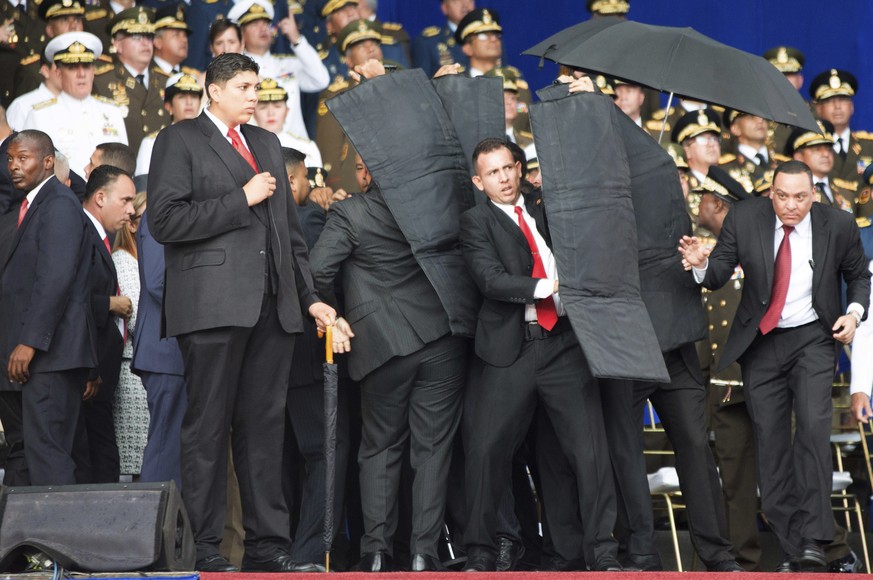 In this photo released by China's Xinhua News Agency, security personnel surround Venezuela's President Nicolas Maduro during an incident as he was giving a speech in Caracas, Venezuela, Saturday, Aug ...