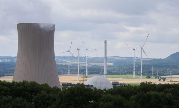 Dampf steigt aus den Kühltürmen des Atomkraftwerk (AKW) Grohnde im Landkreis Hameln-Pyrmont auf, während im Hintergrund Windräder zu sehen sind.