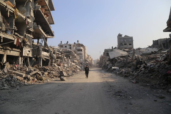 240108 -- GAZA, Jan. 8, 2024 -- A man walks on a street with destroyed buildings in the northern Gaza Strip town of Beit Lahia, on Jan. 8, 2024. The Palestinian death toll from the ongoing Israeli att ...