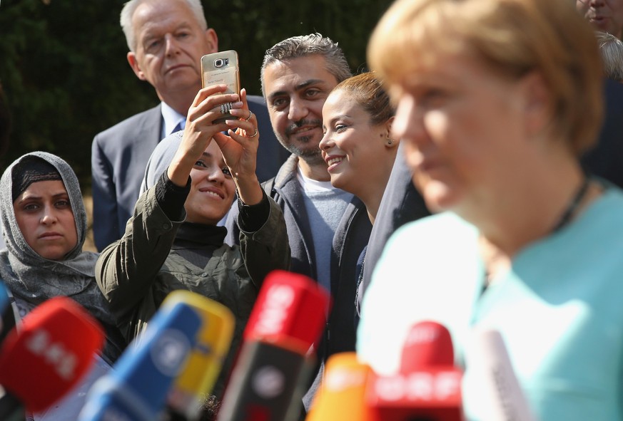 BERLIN, GERMANY - SEPTEMBER 10: Migrants look on as German Chancellor Angela Merkel speaks to the media after she visited the AWO Refugium Askanierring shelter for migrants on September 10, 2015 in Be ...