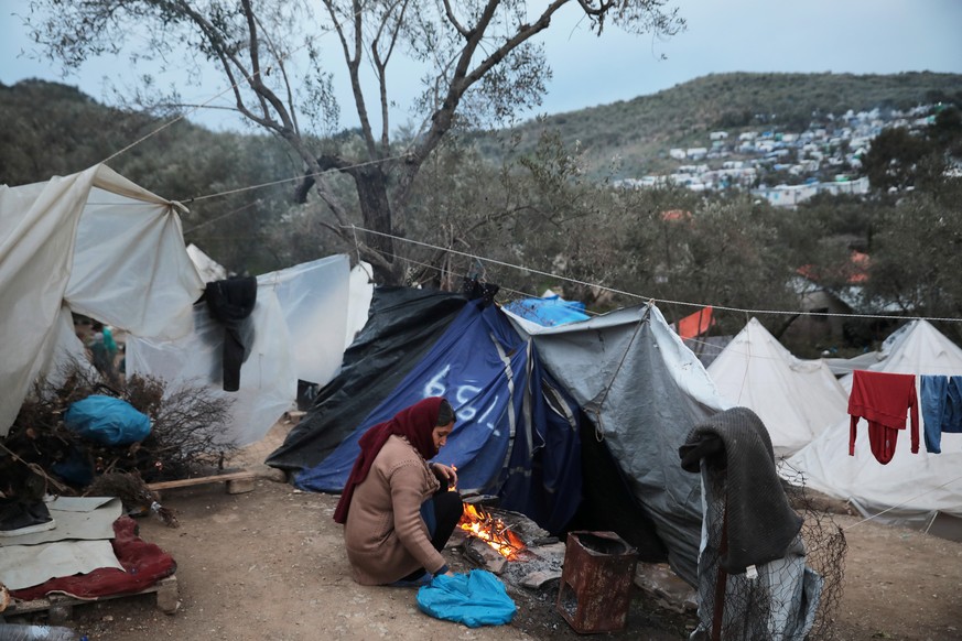 A woman lights up a fire at a makeshift camp for refugees and migrants next to the Moria camp, on the island of Lesbos, Greece, March 7, 2020. REUTERS/Costas Baltas