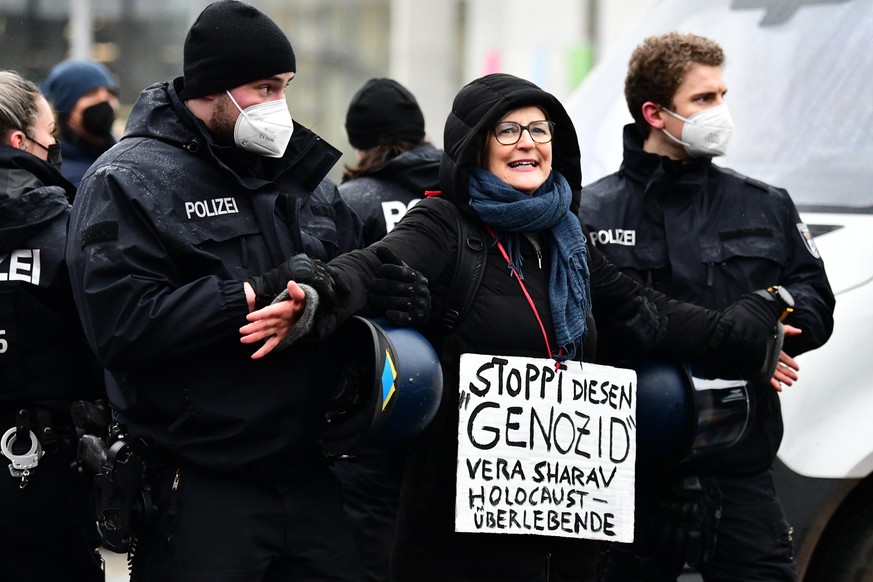 Eine Teilnehmerin wird von Polizisten fest gehalten und trägt ein Schild mit der Aufschrift «Stoppt diesen »Genozid«» und nimmt an einer Demonstration gegen die aktuellen Corona-Maßnahmen und gegen ei ...