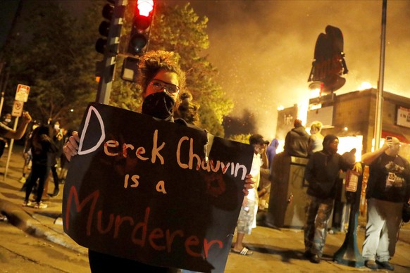 A protester holds a sign in front of a fire at a restaurant, early Friday, May 29, 2020, in Minneapolis. Protests over the death of George Floyd, a black man who died in police custody Monday, broke o ...
