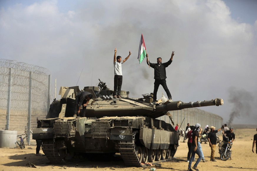 Palestinians wave their national flag and celebrate by a destroyed Israeli tank at the Gaza Strip fence east of Khan Younis southern Saturday, Oct. 7, 2023. The militant Hamas rulers of the Gaza Strip ...