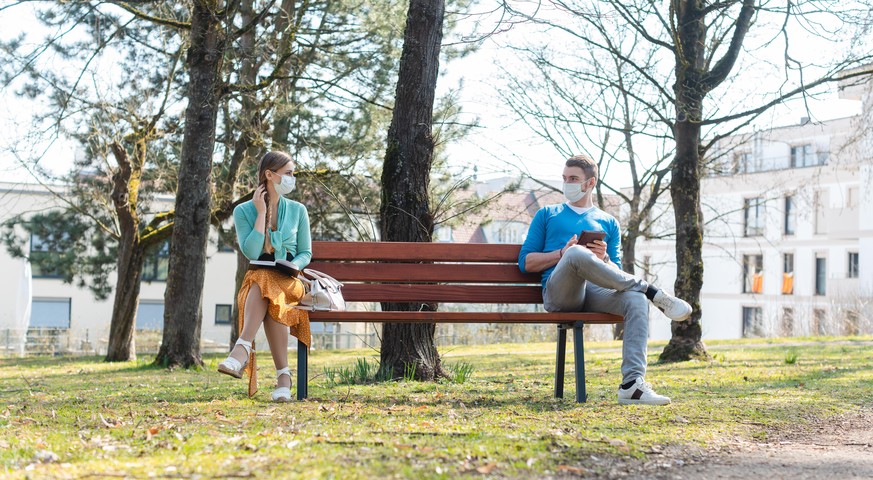 Zwei Menschen sitzen mit Abstand auf einer Parkbank und unterhalten sich.