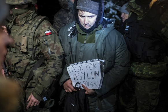 ARCHIV - 01.12.2021, Polen, Harkawicze: Ein Asylbewerber aus Syrien, der von polnischen Grenzbeamten in Gewahrsam genommen wurde, h�lt ein Papier mit der Aufschrift �I ask for asylum in Poland� (�Ich ...