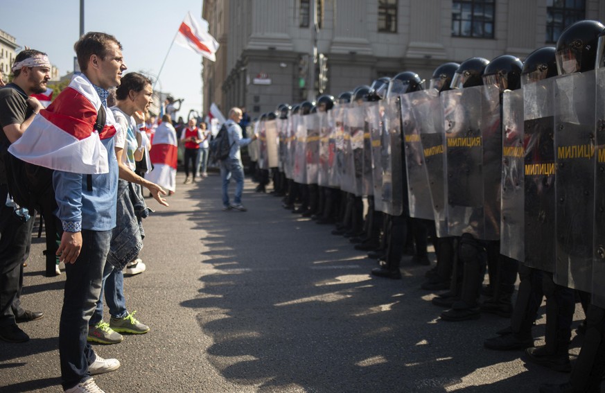 30.08.2020, Belarus, Minsk: Demonstranten mit der ehemaligen belarussischen Nationalflagge und Bereitschaftspolizisten stehen sich w