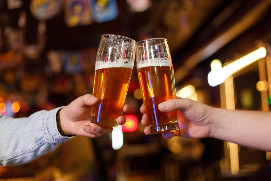 Two glasses of beer clink on st. patrick&#039;s day. Cheerful ginger man wearing a leprechaun hat for st. patrick&#039;s day drinking beer in a pub, ordering a few glasses of beer, getting drunk, havi ...