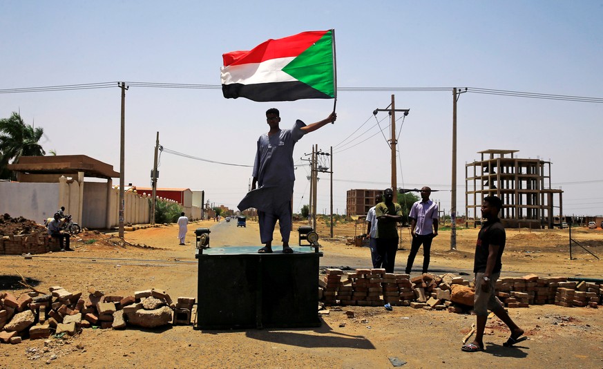 A Sudanese protester holds a national flag as he stands on a barricade along a street, demanding that the country's Transitional Military Council hand over power to civilians, in Khartoum, Sudan June  ...