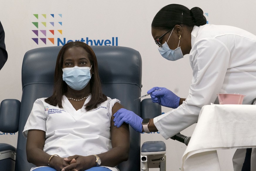 14.12.2020, USA, New York: Krankenschwester Sandra Lindsay (l) wird im Long Island Jewish Medical Center von Dr. Michelle Chester mit dem Corona-Impfstoff des Mainzer Pharma-Unternehmens Biontech und  ...