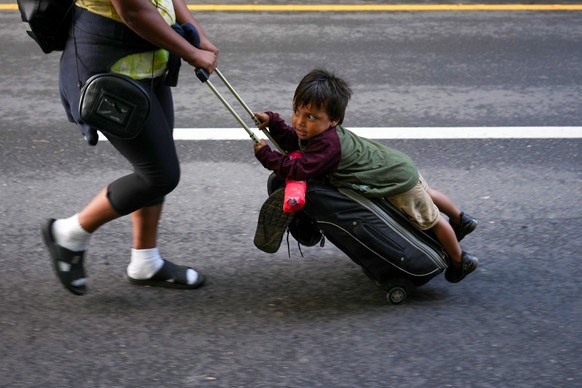 07.11.2024, Mexiko, Huixtla: Ein Kind hält sich an einem Gepäckstück fest, während Migranten auf dem Weg zur Nordgrenze des Landes die Autobahn entlanglaufen, um die USA zu erreichen. Foto: Moises Cas ...