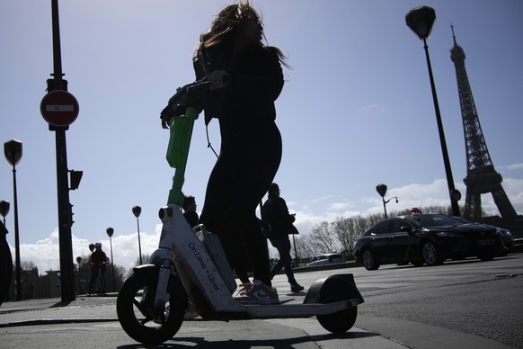 ARCHIV - 30.03.2023, Frankreich, Paris: Eine Frau fährt auf einem E-Scooter. Romantisch zu zweit auf einem Roller, mit Wind in den Haaren, am Eiffelturm und anderen ikonischen Sehenswürdigkeiten vorbe ...