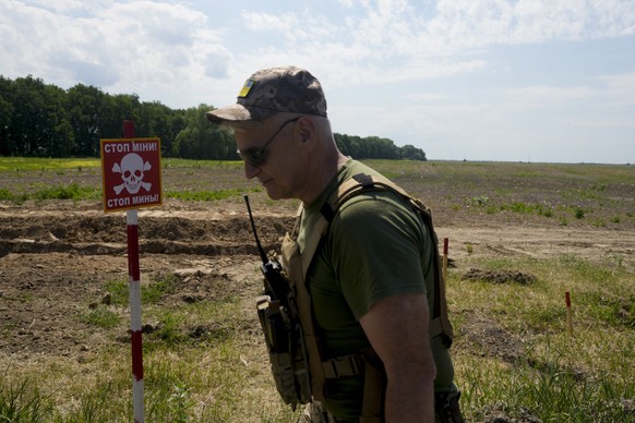 09.06.2022, Ukraine, Kiew: Ein ukrainischer Soldat geht in der Nähe eines Warnpostens vor Landminen auf einem Feld entlang. Foto: Natacha Pisarenko/AP/dpa +++ dpa-Bildfunk +++