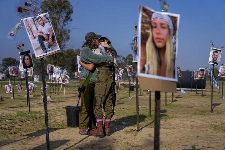 Israeli soldiers embrace next to photos of people killed and taken captive by Hamas militants during their rampage through the Nova music festival in southern Israel, which are displayed at the site o ...