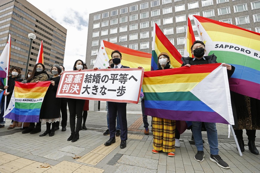 Anwälte der Kläger und Unterstützer halten Regenbogenflaggen und ein Transparent mit der Aufschrift: "Verfassungswidriges Urteil" vor dem Bezirksgericht Sapporo hoch.