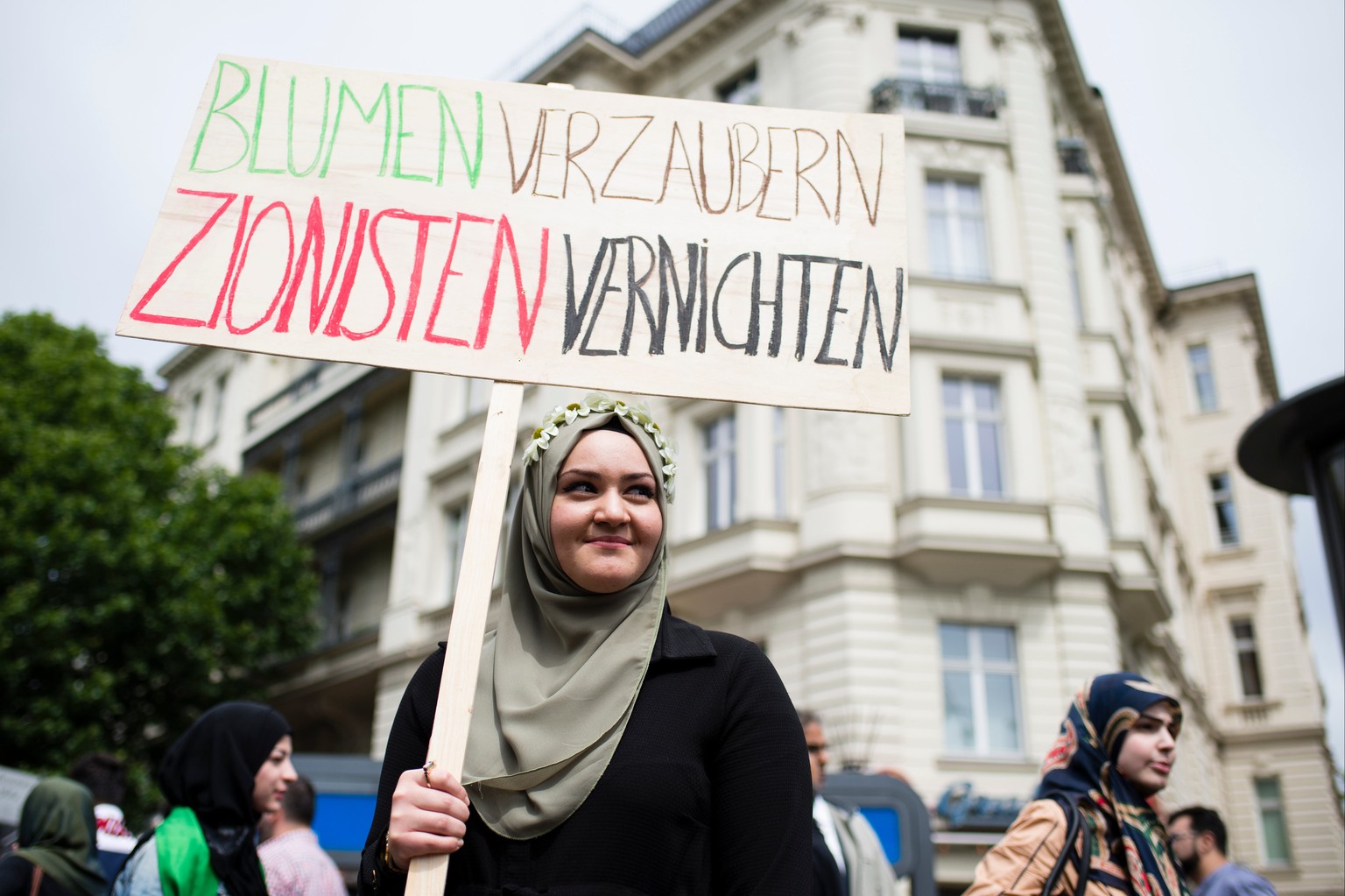 Eine Aktivistin hält am 11.07.2015 ein Schild mit der Aufschrift "Blumen verzaubern, Zionisten vernichten" auf einer Demonstration für Palästina und gegen Zionismus anlässlich des Al-Kuds-Tag in Berli ...