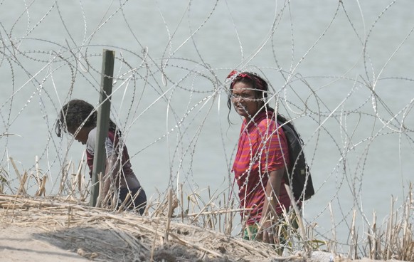USA, Migranten aus Mittelamerika am Rio Grande in Eagle Pass, Texas August 21, 2023, Eagle Pass, TX, United States: A group of migrants look for an opening in the concertina wire barrier south of Eagl ...