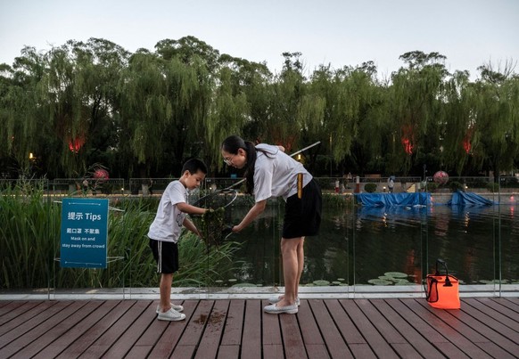 BEIJING, CHINA - JULY 07: A woman and her son check their net as they catch a release small fish from the Liangma River on a hot summer day on July 7, 2022 in Beijing, China. Parts of northern China a ...