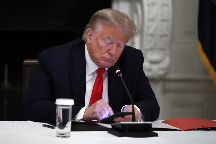 FILE - In this Thursday, June 18, 2020 file photo, President Donald Trump looks at his phone during a roundtable with governors on the reopening of America's small businesses, in the State Dining Room ...