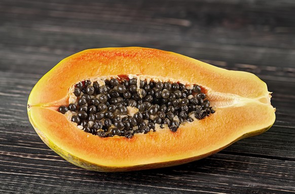 Half papaya on a wooden table. Papaya lies on dark boards with a blurred background.