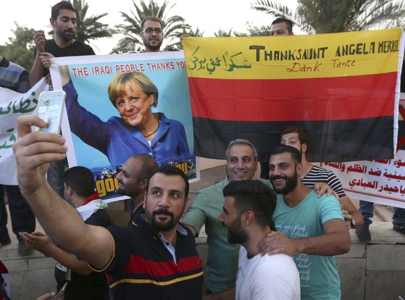 FILE - Iraqi protesters take a selfie with a poster of German Chancellor Angela Merkel and a German flag, during demonstrations against corruption in Tahrir Square in Baghdad, Iraq, Friday, Sept. 4, 2 ...