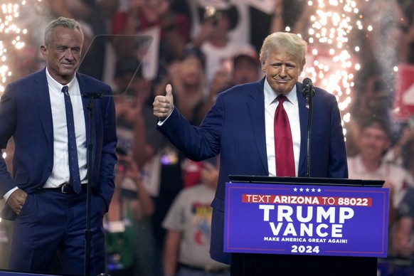 23.08.2024, USA, Glendale: Robert F. Kennedy Jr. (l) sieht zu, wie der republikanische Präsidentschaftskandidat und ehemalige US-Präsident Donald Trump bei einer Wahlkampfveranstaltung spricht. Foto:  ...