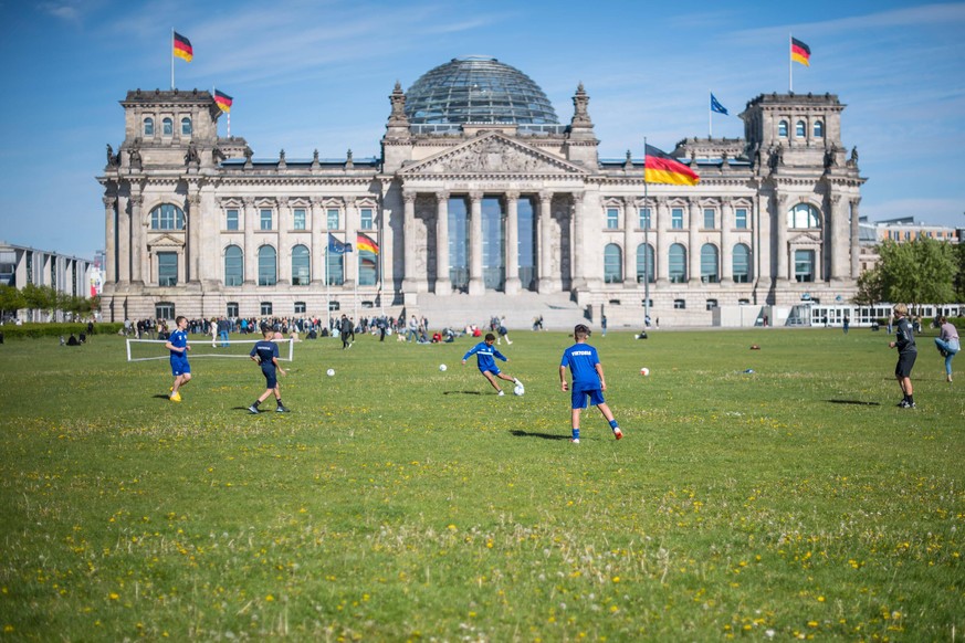 Jugendliche spielen Fußball auf der Wiese vor dem Reichstagsgebäude in Berlin, dem Sitz des Bundestags. 