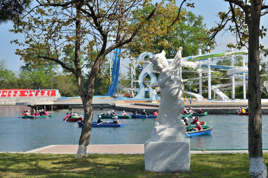 Wonsan, North Korea - May 3, 2019: Inside the Songdowon International Childrens Camp. Funny plaster sculpture of the cartoon character piggy - singer. Children boating in a pond on background