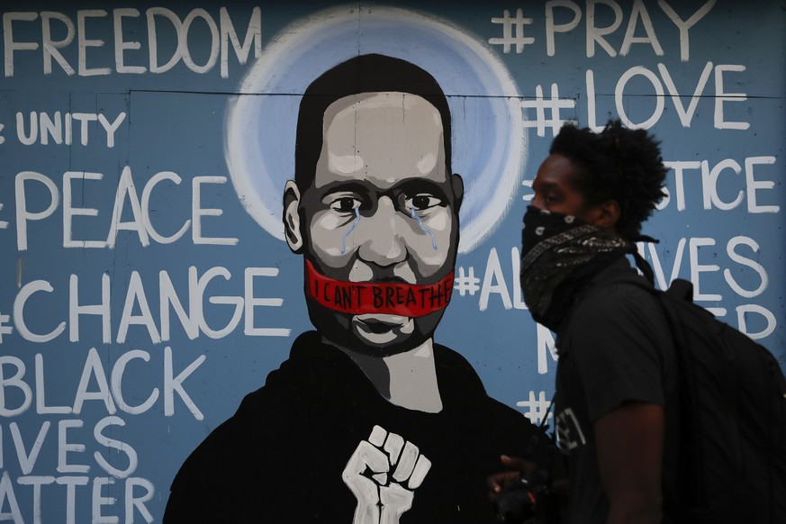 A man with a face covering walks past a mural depicting George Floyd during a protest over the death of Floyd Sunday, May 31, 2020, in Los Angeles. Floyd died in Minneapolis on May 25 after he was pin ...
