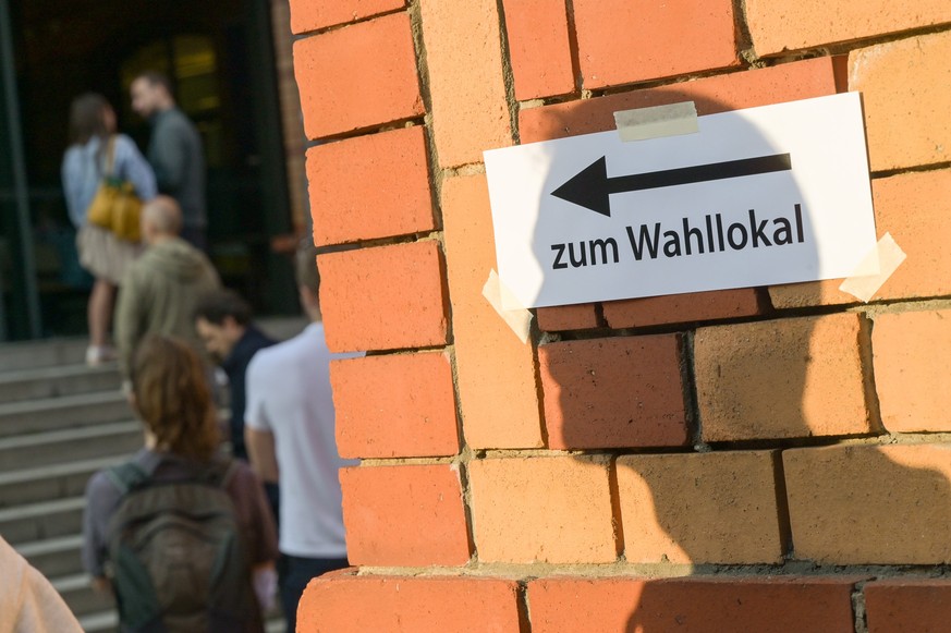 ARCHIV - 26.09.2021, Berlin: W�hlerinnen und W�hler warten vor einem Wahllokal, w�hrend auf einer Mauer davor der Schatten eines Mannes auf einen Zettel mit der Aufschrift �Zum Wahllokal� f�llt. (zu d ...