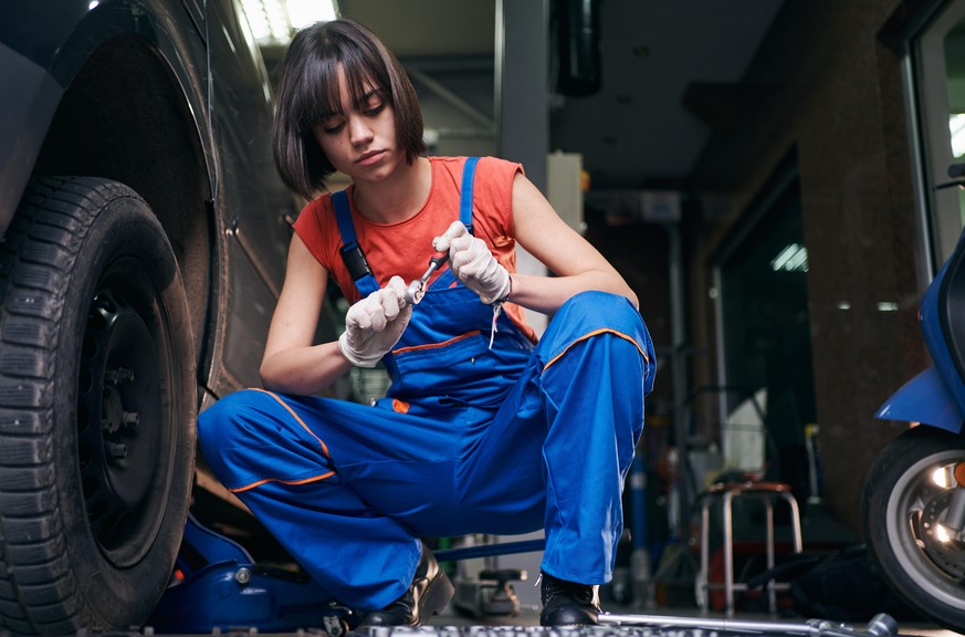 Teenage female mechanic working hard on repairing a tire