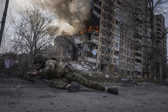 ARCHIV - 17.03.2023, Ukraine, Awdijiwka: Dieses von der Nachrichtenagentur AP am 21.03.2023 zur Verfügung gestellte Foto zeigt einen ukrainischen Polizisten, der vor einem brennenden Gebäude in Deckun ...