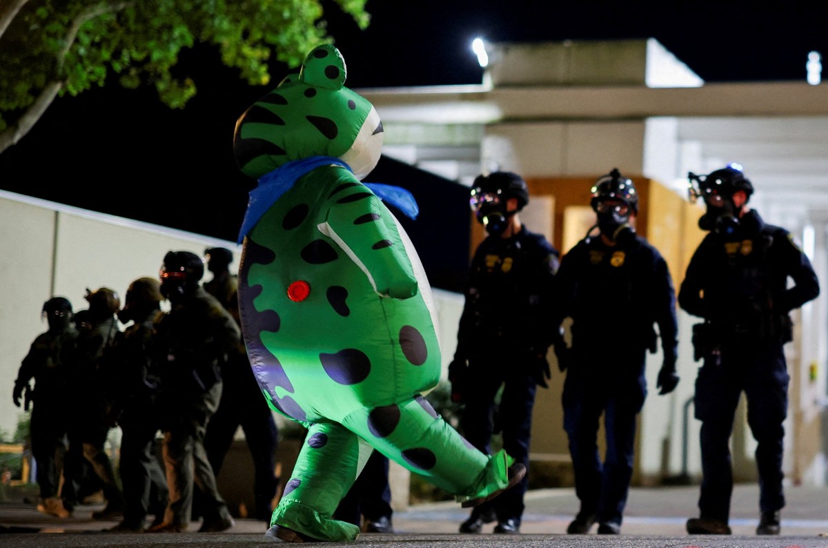 A demonstrator wearing an inflatable frog costume walks outside the U.S. Immigration and Customs Enforcement (ICE) headquarters, as law enforcement officers work to disperse the crowd to clear traffic ...