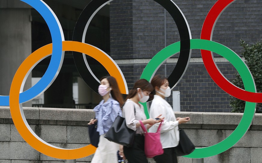 08.07.2021, Japan, Tokio: Menschen mit Gesichtsmasken gehen an der Statue der Olympischen Ringe in Tokio vorbei. Japan wird Tokio ab n