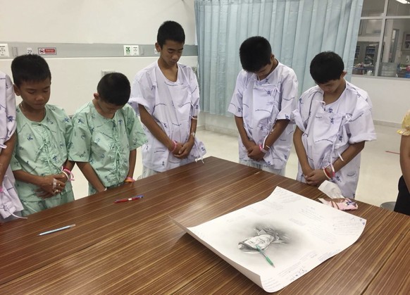 In this photo released by Thailand's Ministry of Health and the Chiang Rai Prachanukroh Hospital, some of the rescued soccer team members bowing their heads respectfully in front of a sketch of the Th ...