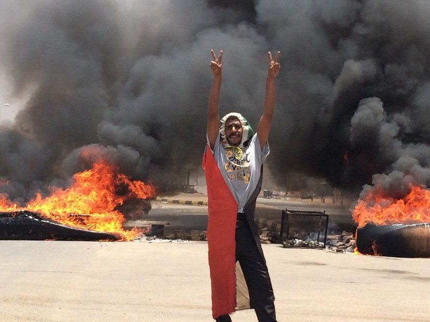 A protester flashes the victory sign in front of burning tires and debris on road 60, near Khartoum's army headquarters, in Khartoum, Sudan, Monday, June 3, 2019. Sudanese protest leaders say at least ...