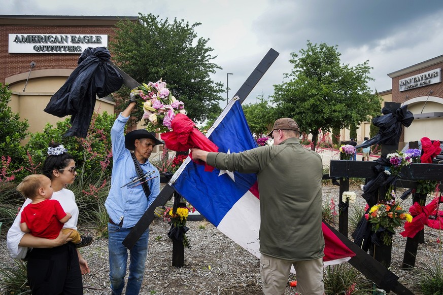 Roberto Marquez, left with hat, and Fred Lowstetter raise a cross with a Texas flag as they construct a memorial outside an entrance to the mall a day after a mass shooting at Allen Premium Outlets on ...