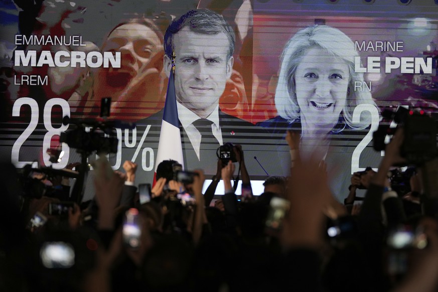 A screen shows French President Emmanuel Macron and centrist candidate for reelection and far-right candidate Marine Le Pen at her election day headquarters, in Paris, Sunday, April 10, 2022. French p ...