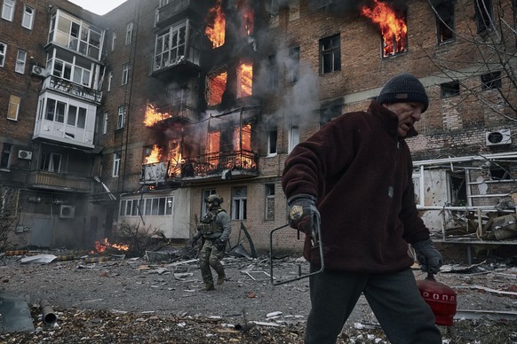 07.12.2022, Ukraine, Bachmut: Ein Anwohner verl�sst sein Wohnhaus, das nach einem Beschuss in Flammen steht. Foto: Libkos/AP/dpa +++ dpa-Bildfunk +++