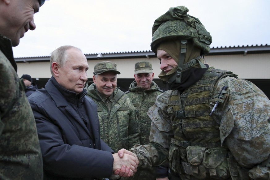 ARCHIV - 20.10.2022, Russland, Rjasan: Der russische Präsident Wladimir Putin schüttelt einem Soldaten die Hand, und der russische Verteidigungsminister Sergej Schoigu steht lächelnd neben ihm, währen ...