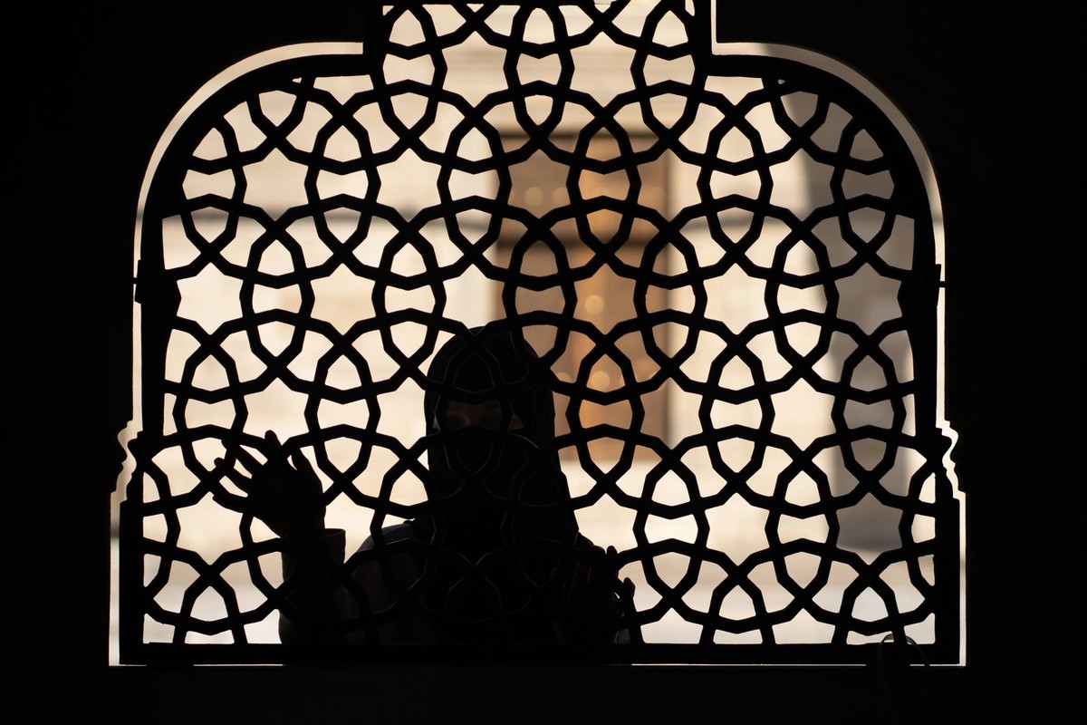A Muslim girl in a black hijab stands behind a patterned wrought-iron fence. Woman in a conservative Arab country.