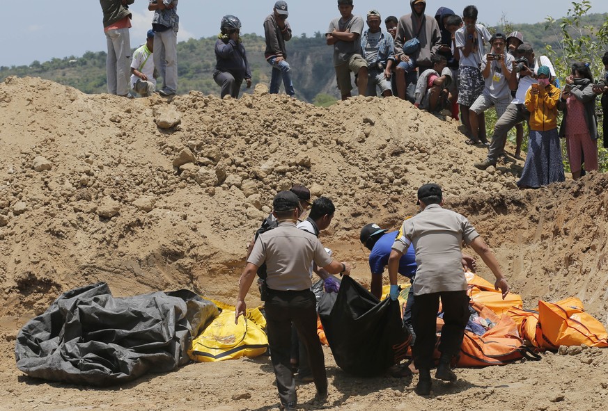 Rescue teams carry the bodies of victims to a mass grave following a major earthquake and tsunami in Palu, Central Sulawesi, Indonesia, Monday, Oct. 1, 2018. A mass burial of earthquake and tsunami vi ...